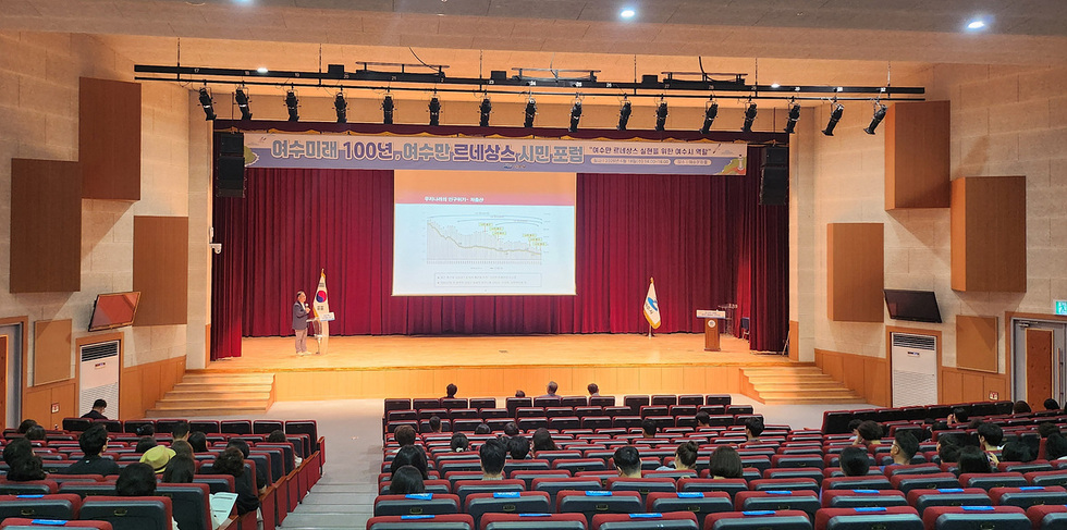 어수미래 100년 어수만 르네상스 시민포럼이 진행되고 있는 강당에서 발표자가 화면을 보이며 설명하고 있다. 청중들이 발표를 경청하고 있다.