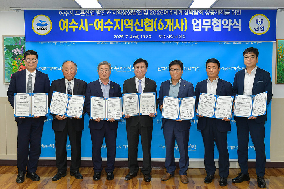 여수시청 시장실에서 여수시와 여수지역신협 간의 업무협약식이 진행되고 있다. 참석자들이 협약서를 들고 서 있다.