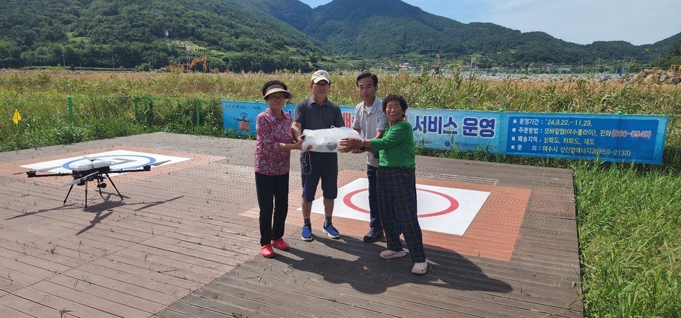 섬 주민들이 드론을 통해 배송된 생활 물품을 전달받고 함께 기념사진을 찍는 모습