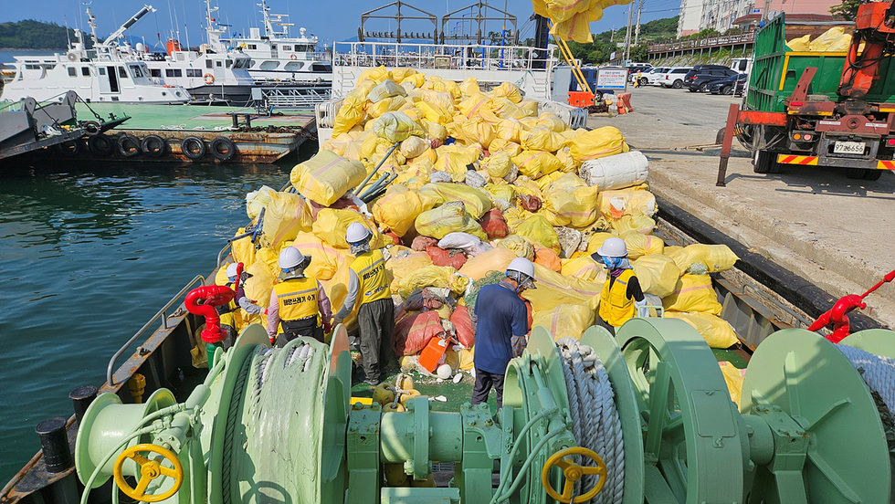 해양쓰레기를 수거하는 작업자들이 노란색 봉투로 가득 찬 배 위에서 작업하고 있는 모습이다.