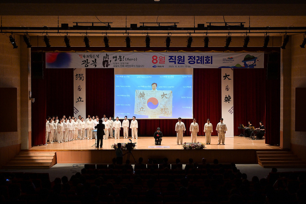 무대에서 여러 명의 사람들이 흰색 의상을 입고 공연을 하고 있으며, 화면에는 한국 국기와 관련된 내용이 표시되고 있다.