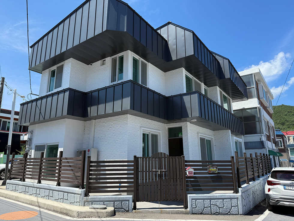 흰색 벽과 검은색 지붕을 가진 3층 건물이 도로에 면해 있으며, 주변에 다른 건물들이 보인다. 건물 앞에는 나무 울타리가 설치되어 있다.