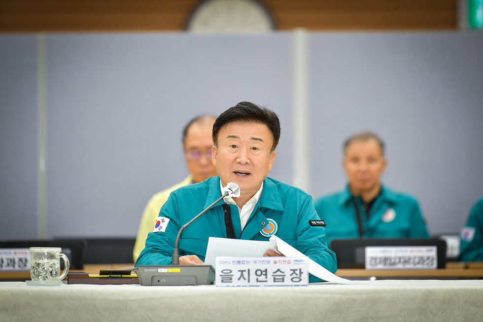 을지연습장에서 회의를 진행하는 모습으로, 발언하는 남성이 있으며 배경에는 다른 참석자들이 보인다.