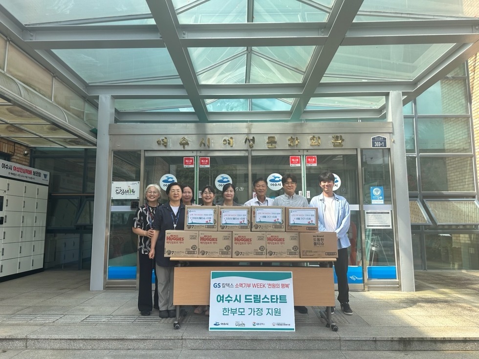 여수시 드림스타트 지원을 위한 행사에서 여러 사람이 상자 앞에 서 있다. 상자에는 아기 기저귀가 담겨 있으며, 배경에는 여수시 여성가족부 건물이 보인다.