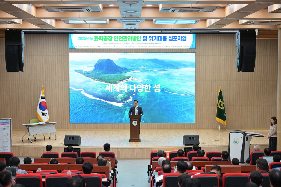 2025년도 화학공장 안전관리방안 및 위기대응 심포지엄이 진행되고 있으며, 연단에서 발표자가 서 있고 배경에는 다양한 섬을 보여주는 화면이 있다.