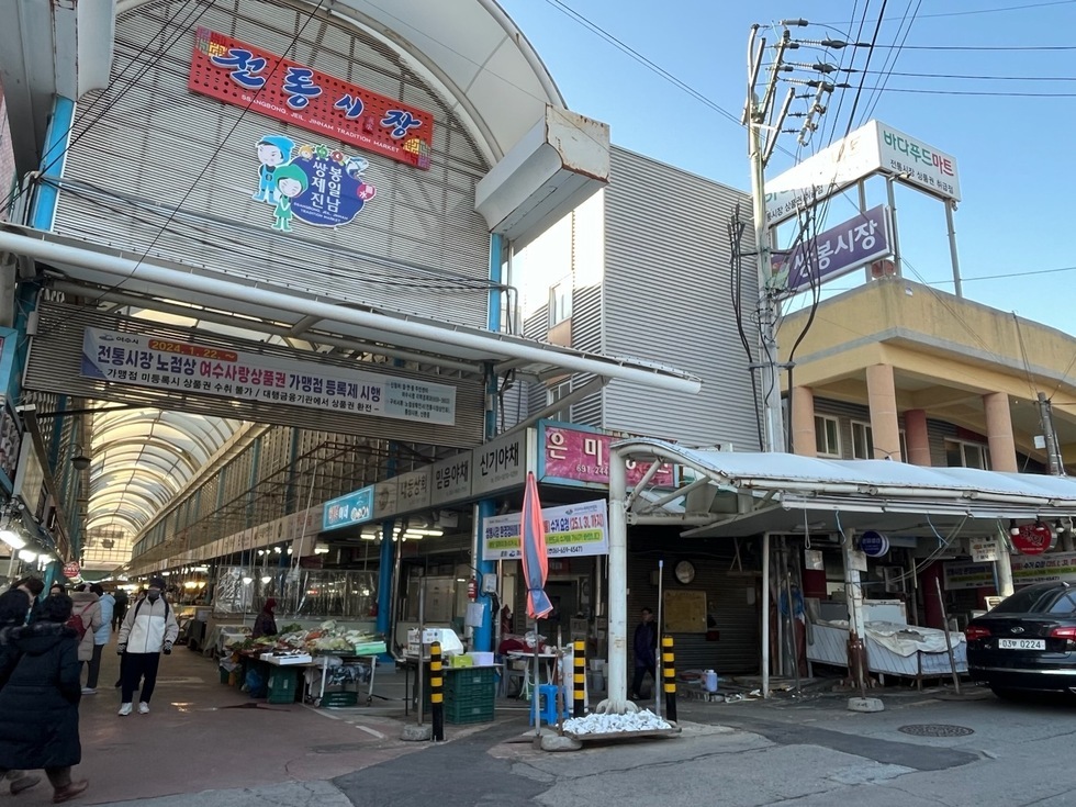 여수의 전통시장에서 상점들이 줄지어 있는 모습으로, 노점상과 가맹점 등록제 시행을 알리는 현수막이 걸려 있다.