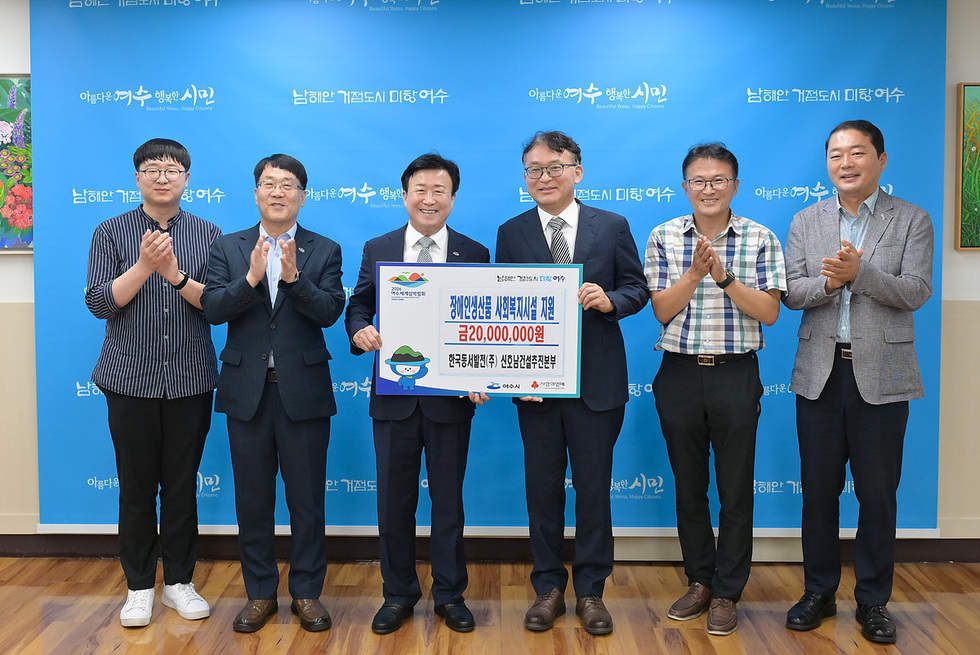 여수시에서 장애인 생산품 사회복지시설 지원을 위한 기념사진 촬영 장면으로, 여러 명의 관계자가 함께 모여 지원금 전달식을 진행하고 있다.