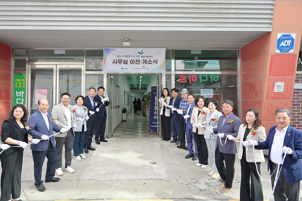 여수시 식전동에서 사무실 이전 개소식이 진행되고 있으며, 여러 사람들이 리본을 들고 기념사진을 찍고 있다.