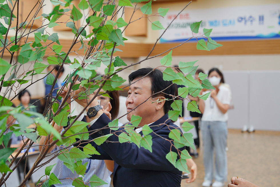 한 남성이 나무 가지를 다듬고 있으며, 배경에는 여러 사람이 관찰하고 있는 모습이 보인다.