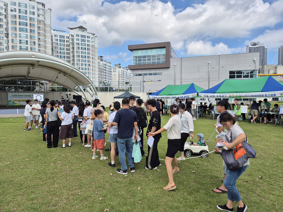 사람들이 아동청소년 정신건강축제에 참여하기 위해 줄을 서 있는 모습으로, 행사장에는 여러 부스와 무대가 보인다.