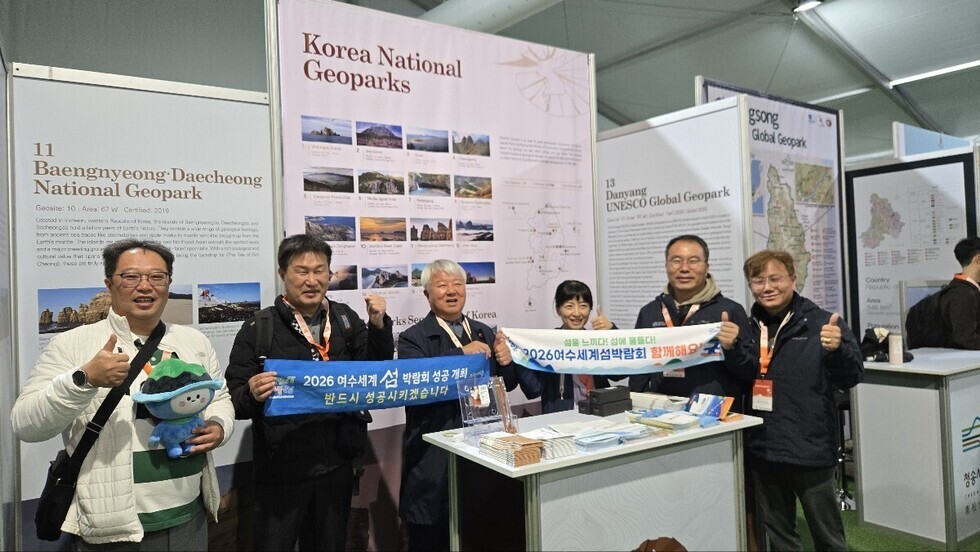 한국관 지질공원 홍보 부스 앞에서 여수시 관계자들이 2026여수세계섬박람회 홍보 문구가 적힌 현수막을 들고 기념사진을 찍으며 엄지손가락을 치켜세우고 있는 모습.