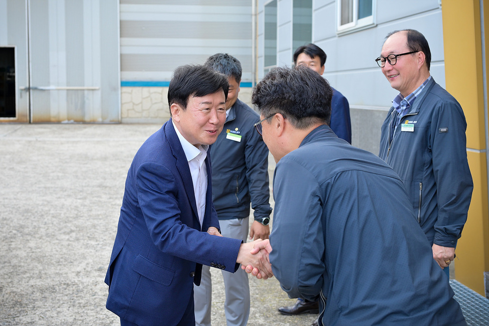 정기명 여수시장이 기업 방문 현장에서 관계자와 웃으며 악수하며 인사를 나누고 있는 모습, 옆에는 임직원들이 지켜보고 있다.