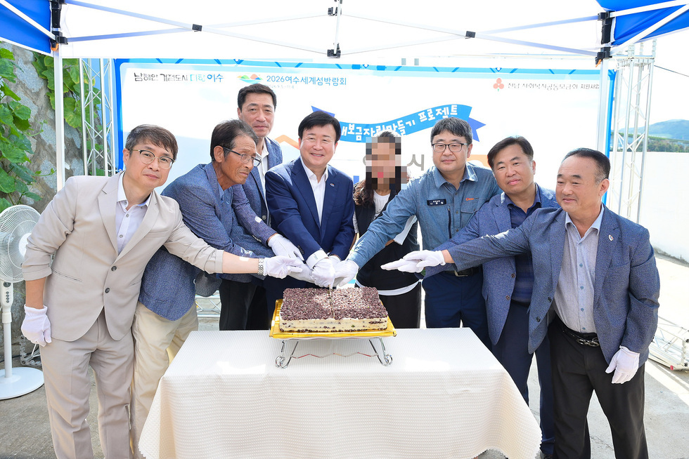 여수시와 후원 기관 관계자들이 희망하우스 28호 준공을 기념하며 흰 장갑을 낀 손으로 함께 케이크를 자르고 환하게 웃고 있는 모습.