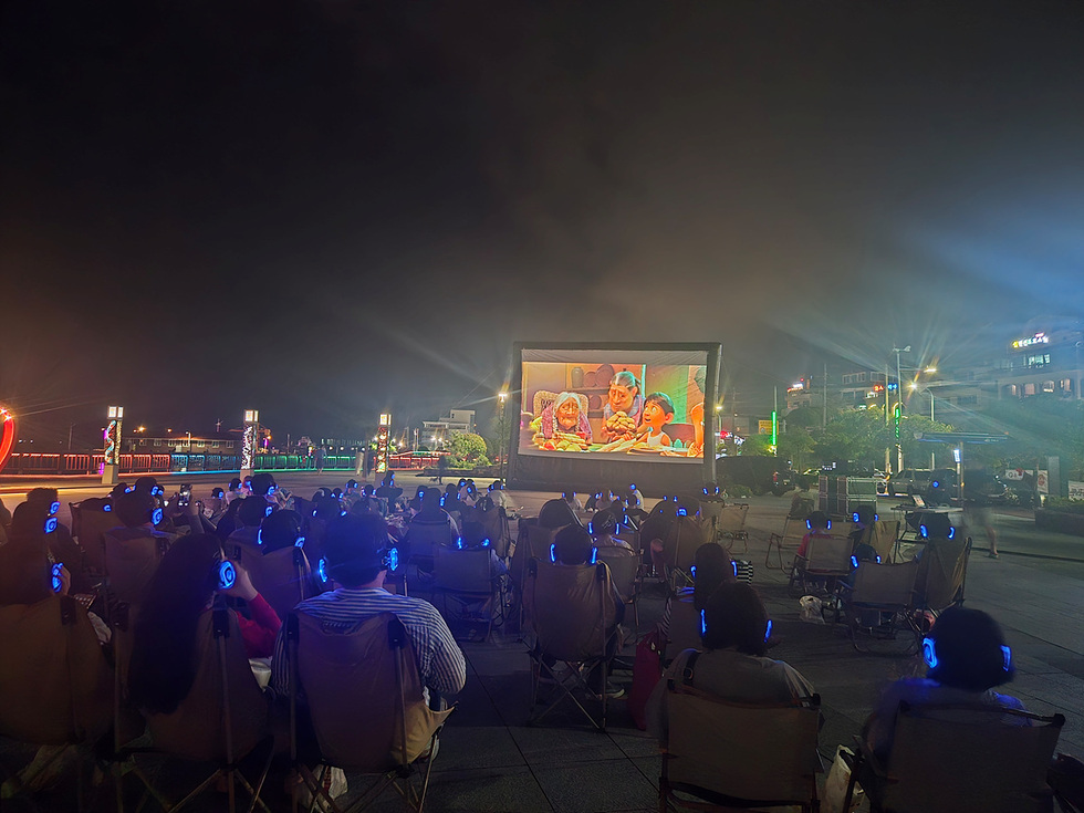 여수 소호동동다리 대광장에서 시민과 관광객들이 야외 영화 상영을 즐기고 있는 모습으로, 애니메이션 코코가 상영되고 있다.