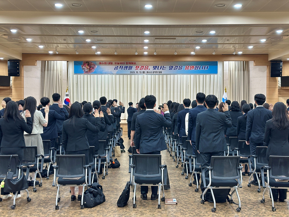 여수시청 회의실에서 신규 공무원들이 임용장 수여식에 참석하여 손을 들어 선서하고 있는 모습