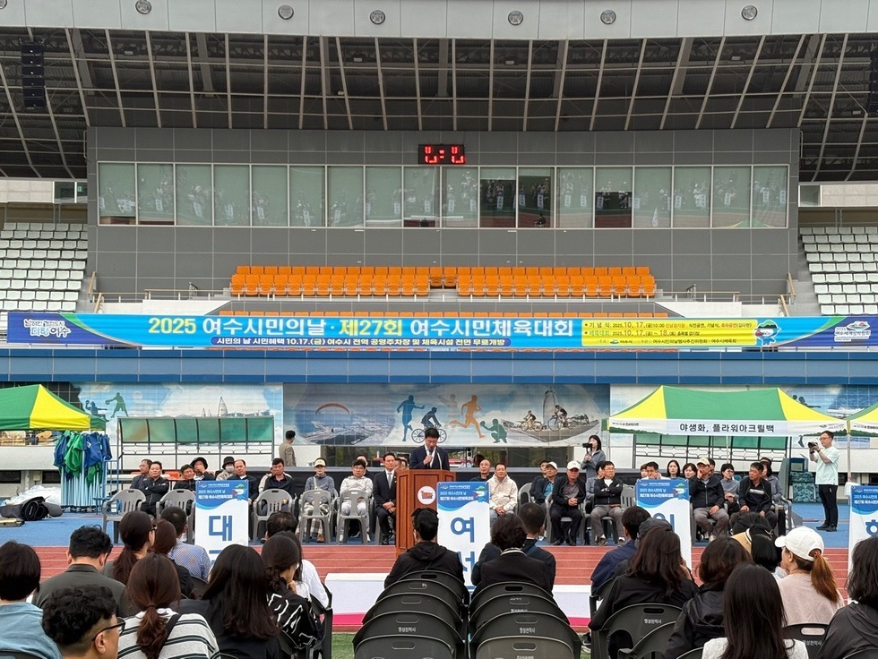 여수시민의 날 기념 제27회 시민체육대회 개회식에서 연단에 서 있는 진행자와 참석한 시민들이 보인다.