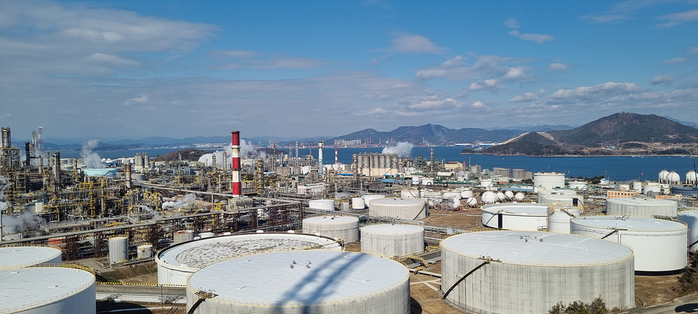 여수시의 석유화학 산업 단지 전경으로, 대형 저장탱크와 공장 시설이 보이며 배경에는 바다와 산이 보인다.