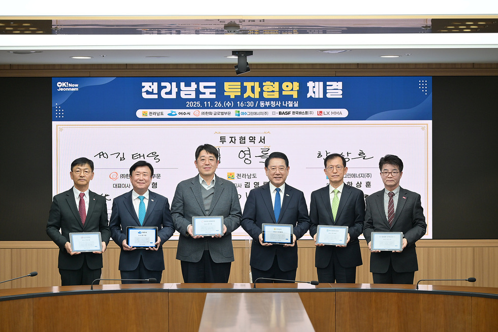 전라남도 투자협약 체결식에서 여섯 명의 참석자가 협약서를 들고 단상 앞에 서서 기념촬영하고 있다. 뒤편 전광판에는 ‘전라남도 투자협약 체결’ 문구와 일정이 표시돼 있다.